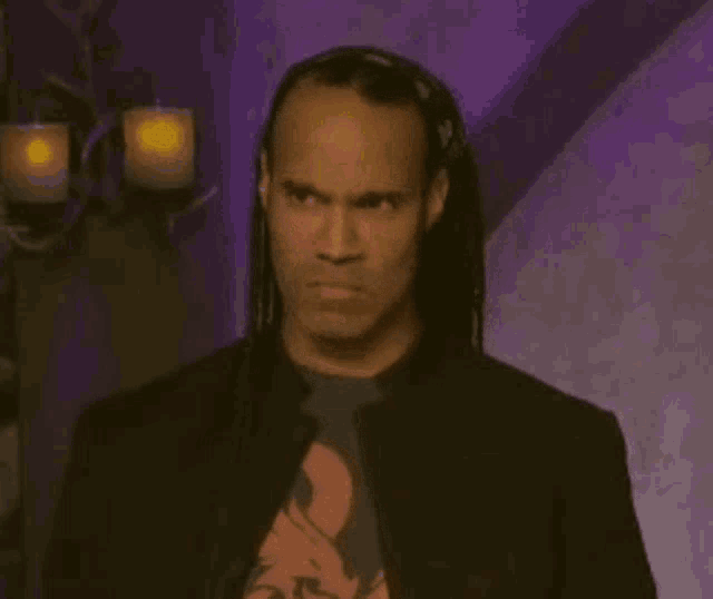 a man with long hair is wearing a black jacket and tie .