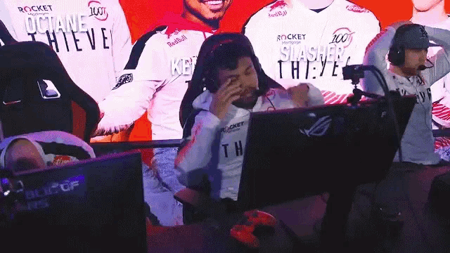 a man wearing a white octane thieve shirt is sitting in front of a computer