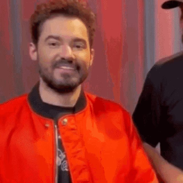 a man with a beard and a red jacket is smiling .