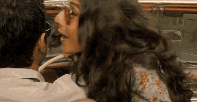 a man and a woman are kissing in a car . the woman is wearing sunglasses .