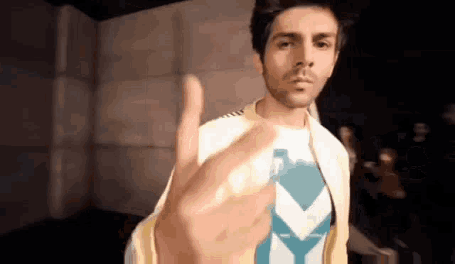 a man is giving a thumbs up sign while wearing a yellow jacket and a blue shirt .
