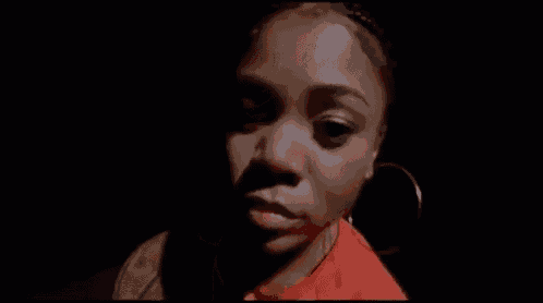 a close up of a woman 's face with a black background . she is wearing hoop earrings and a red shirt .