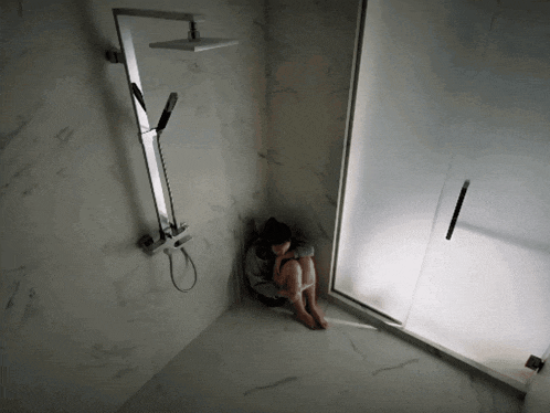 a woman sits in a corner of a bathroom next to a shower