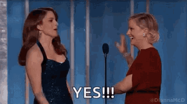two women are standing next to each other in front of a microphone . one of the women is saying yes .