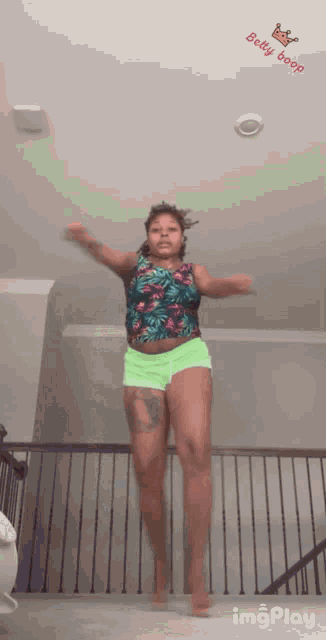 a woman in neon green shorts is jumping in the air with a baby boop sticker on the ceiling