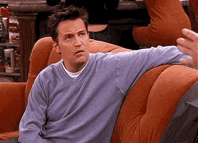 a man in a blue sweater is sitting on a couch with his arms crossed .