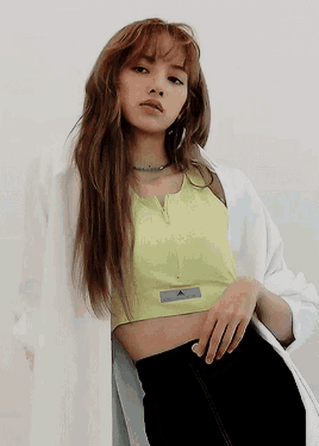 a woman in a yellow crop top and black pants is leaning against a wall