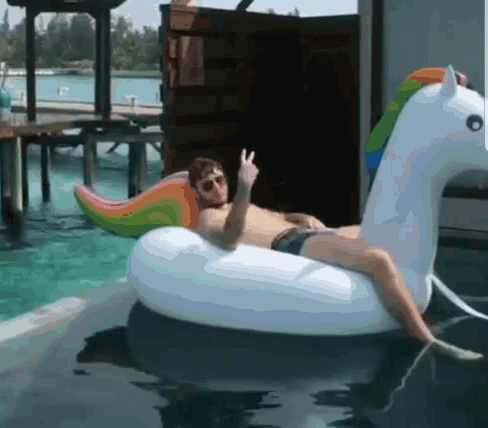 a man is laying on an inflatable unicorn in a pool and giving a peace sign