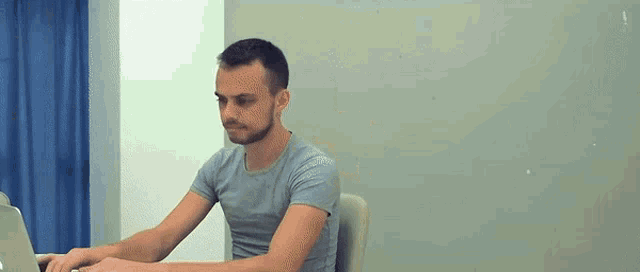 a man is sitting at a desk typing on a laptop .