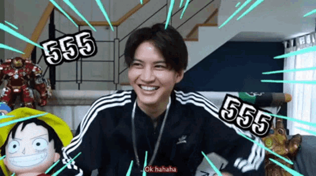 a man wearing a black adidas jacket is smiling and laughing with the number 555 behind him