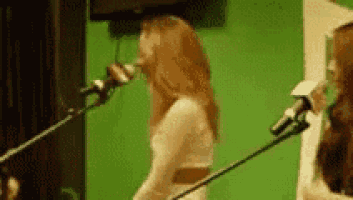 a woman is singing into a microphone while another woman plays a guitar .