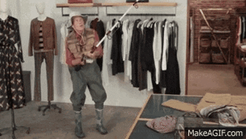 a man in a cowboy hat is holding a fishing rod in a clothes store