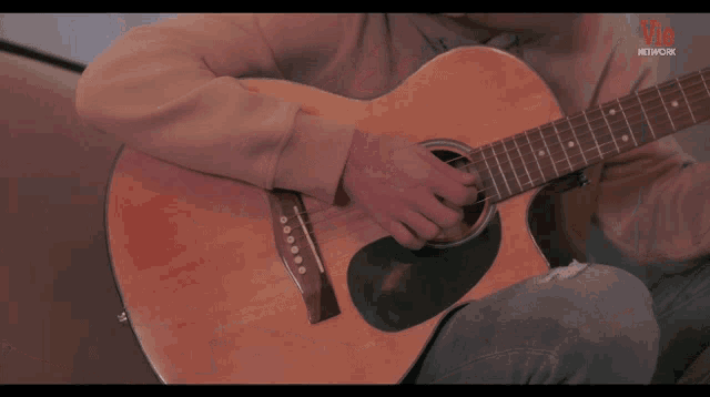 a young man is playing a guitar in front of a vie network sign