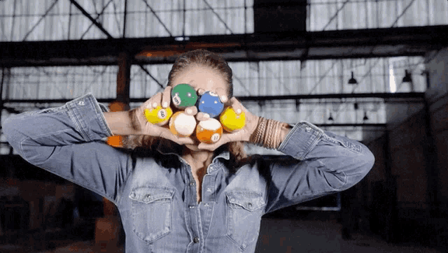 a woman in a denim shirt holds pool balls in front of her eyes
