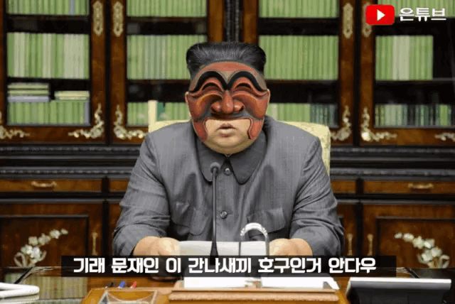 a man wearing a mask sits at a desk in front of a microphone with a youtube logo in the background