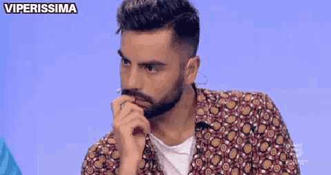 a man with a beard is sitting at a table with his hand on his mouth .