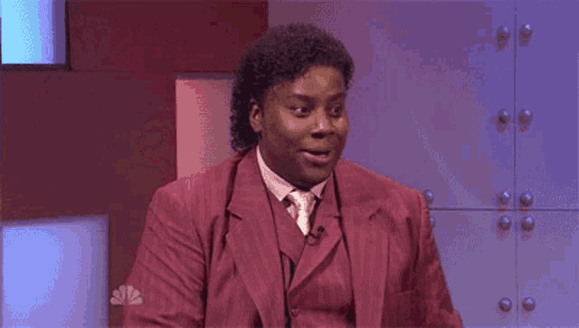 a man in a red suit and tie is sitting in front of a microphone with his mouth open .
