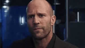 a bald man with a beard is standing in a room and looking at the camera .