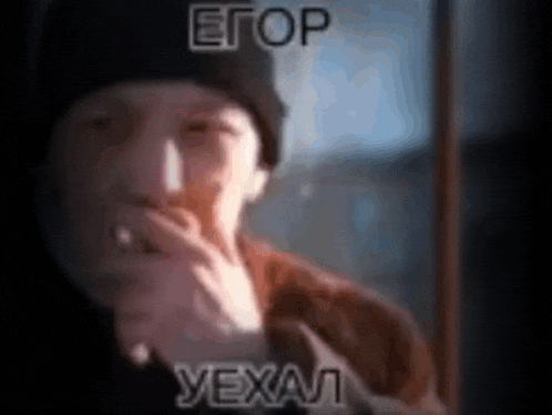 a man is smoking a cigarette while looking out a window and the words etop yexal are on the screen .