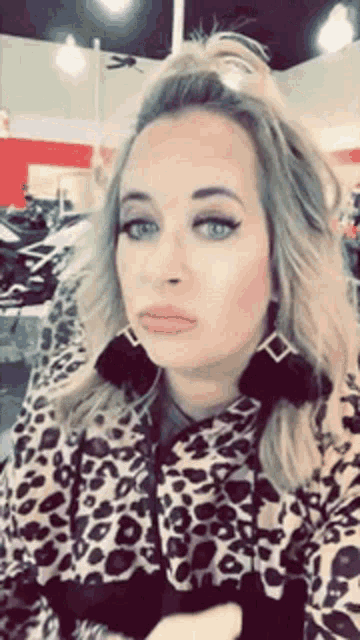 a woman wearing a leopard print jacket and earrings is taking a selfie in a store .