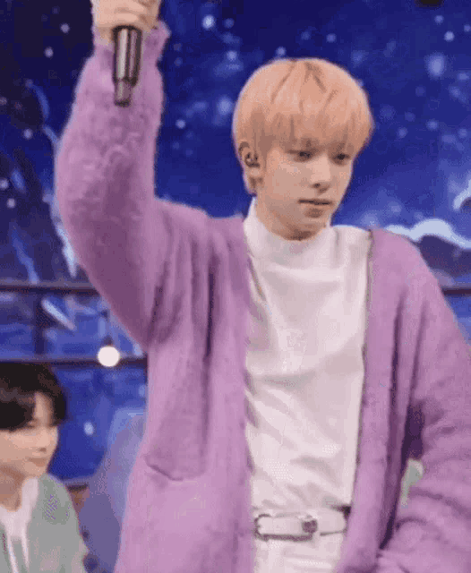 a young man wearing a purple cardigan is holding a microphone in his hand .