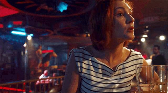 a woman in a striped shirt sits at a bar holding a beer