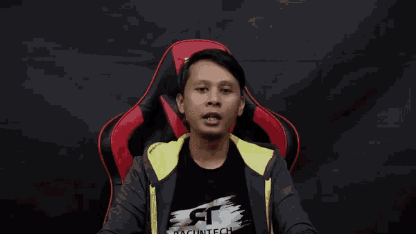 a man wearing a pacuntech shirt sits in a red and black gaming chair