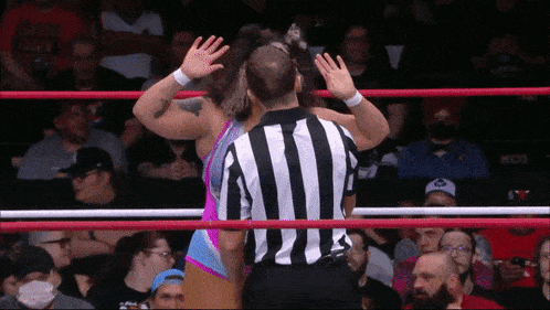 a man in a black and white striped shirt is standing in a wrestling ring
