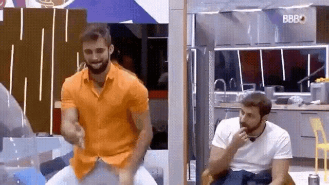 a man in an orange shirt is sitting on another man 's shoulders .