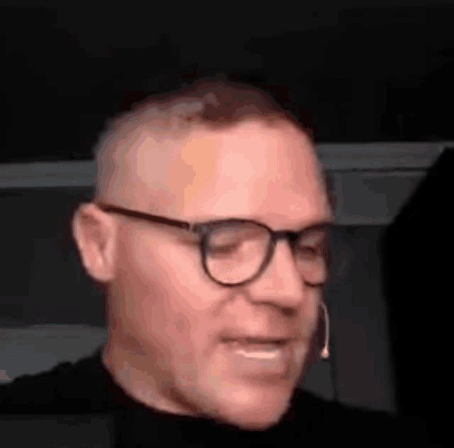 a man wearing glasses and a microphone is smiling and talking on a video call .