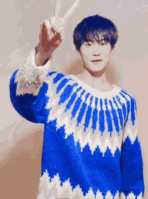 a young man wearing a blue and white sweater giving a peace sign