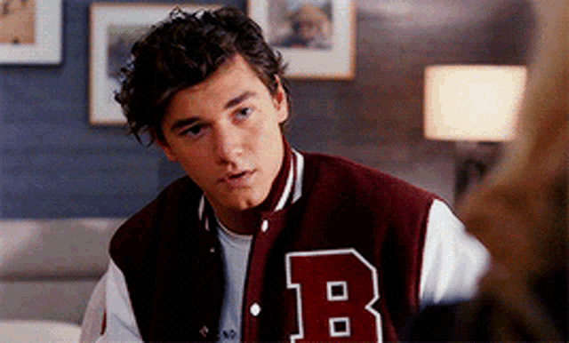 a young man wearing a maroon varsity jacket with the letter b on the front