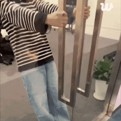 a person in a striped shirt and jeans is opening a glass door