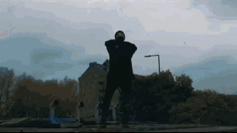 a man in a mask is standing in front of a building and trees .