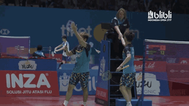 two badminton players giving each other a high five in front of an inza sign
