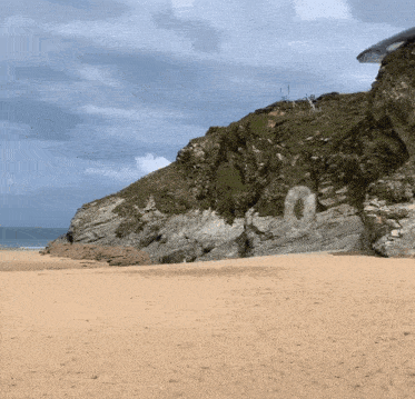 a sandy beach with a cliff in the background and the letter o on the rock