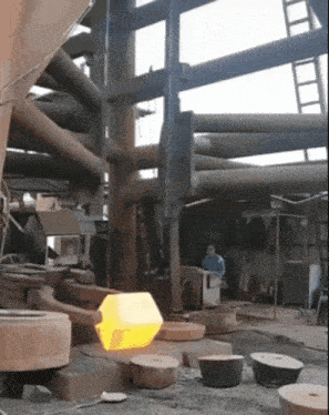 a man sits at a table in a factory with a large yellow object in the background