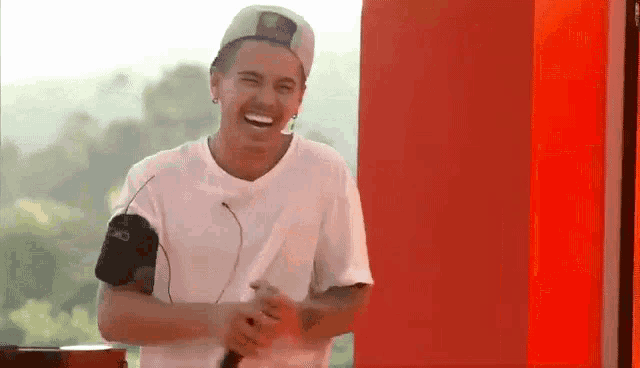 a man wearing a hat and a white shirt is laughing and holding a microphone .