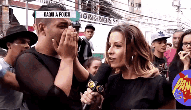 a man is covering his mouth while a woman holds a microphone with the words daqui a pouco on the screen