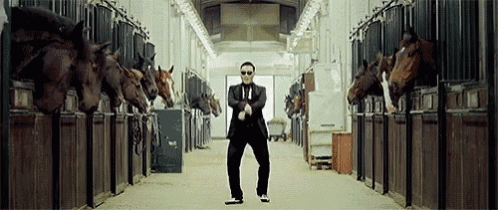a man in a suit is dancing in front of a row of horses in a stable .