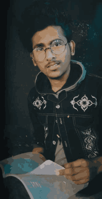 a young man wearing glasses holds a piece of paper
