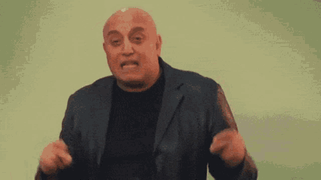 a bald man in a suit and black shirt is making a funny face and dancing .