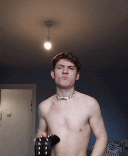 a shirtless man with a necklace around his neck holds a black belt