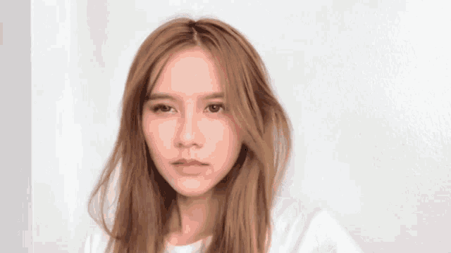 a woman with long brown hair is wearing a white shirt and looking at the camera