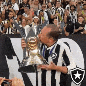 a man in a striped shirt kisses a trophy in front of a crowd