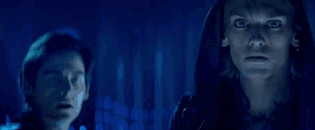 a man in a hooded jacket is standing next to a woman in a dark room