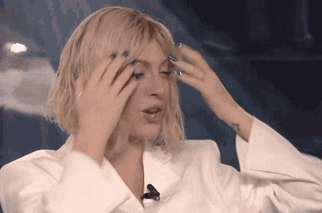 a woman with blonde hair and blue nail polish is covering her face with her hands .