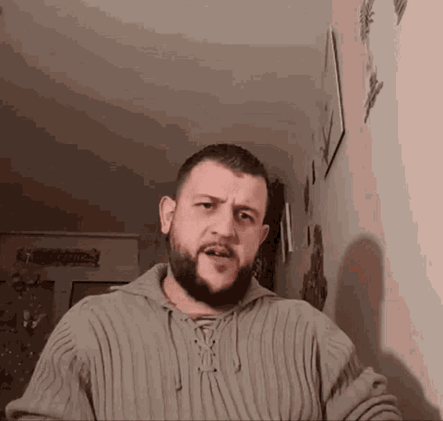 a man with a beard is wearing a sweater and making a face