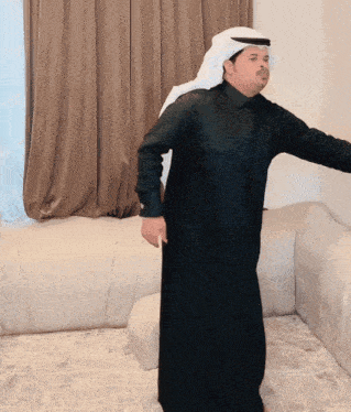 a man wearing a black robe and a white head scarf stands in front of a couch