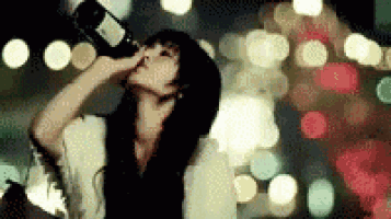 a woman is drinking a bottle of wine in front of a blurry background